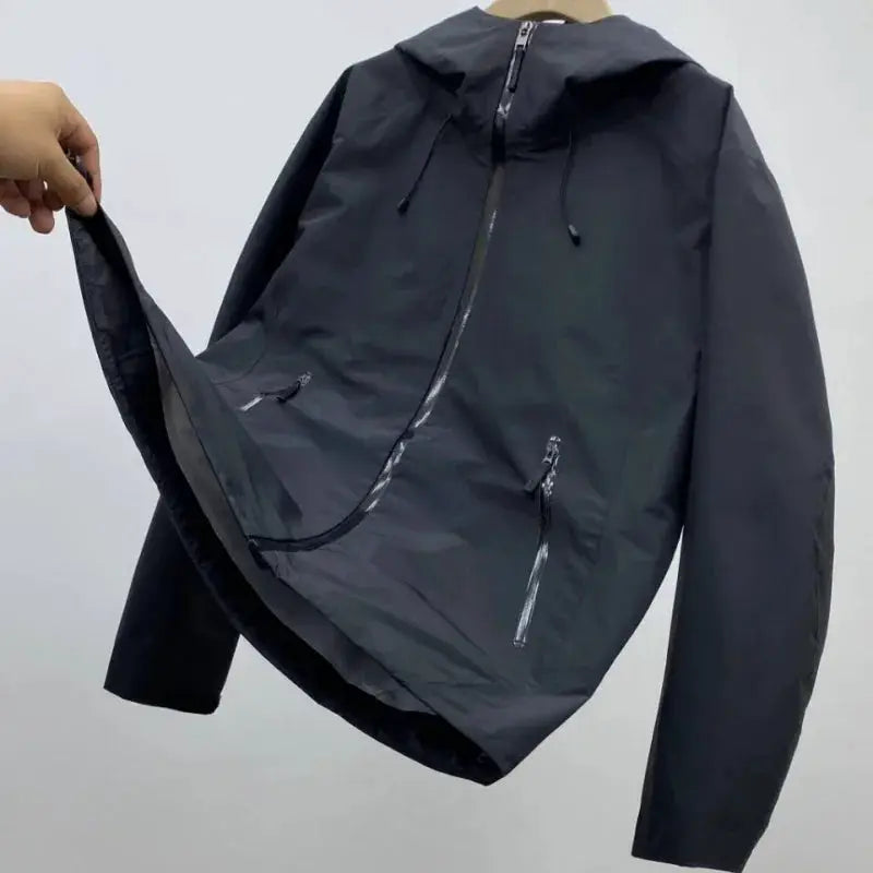 Simples Market men's windproof soft-shell outdoor jacket in dark gray with hood, front zipper, and zip pockets.