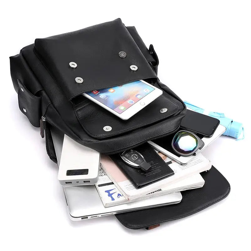 Backpack black PU leather, large laptop backpack with front flap and metal studs, shown with phone, tablet and accessories spilling out.