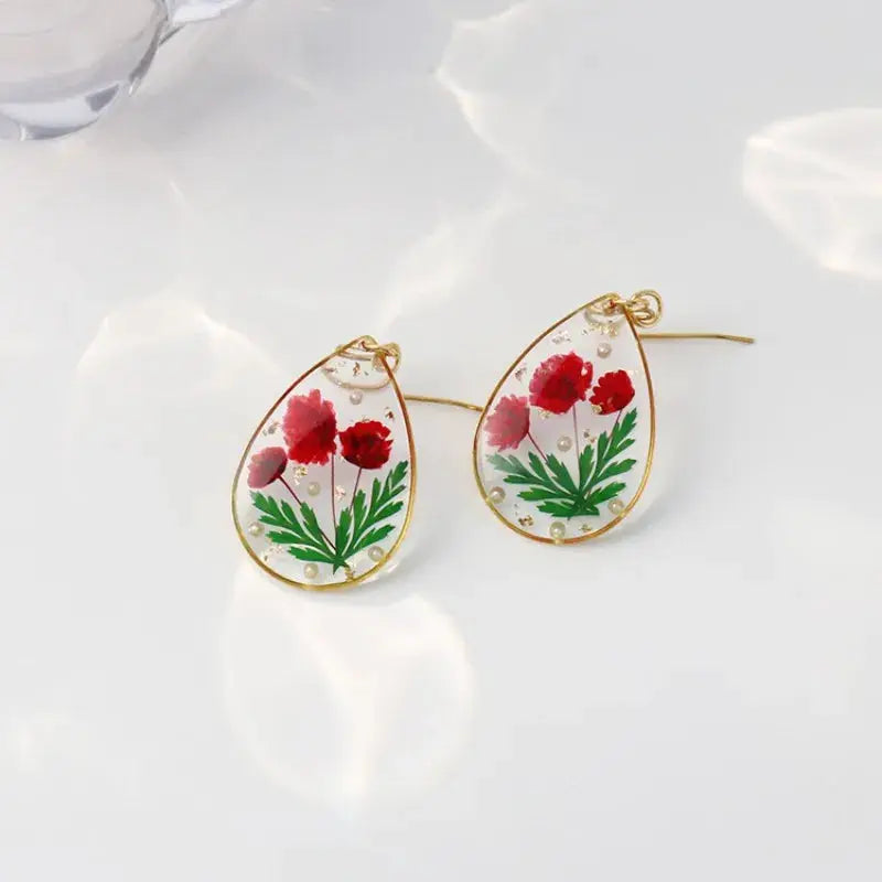 Teardrop epoxy resin earrings (pair) by Simples Market with pressed red flowers and green leaves, gold-tone frame