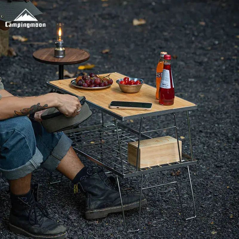 CampingMoon aluminum lunch box for open-flame camping, outdoor picnic setup with wooden table and two plates of fruit