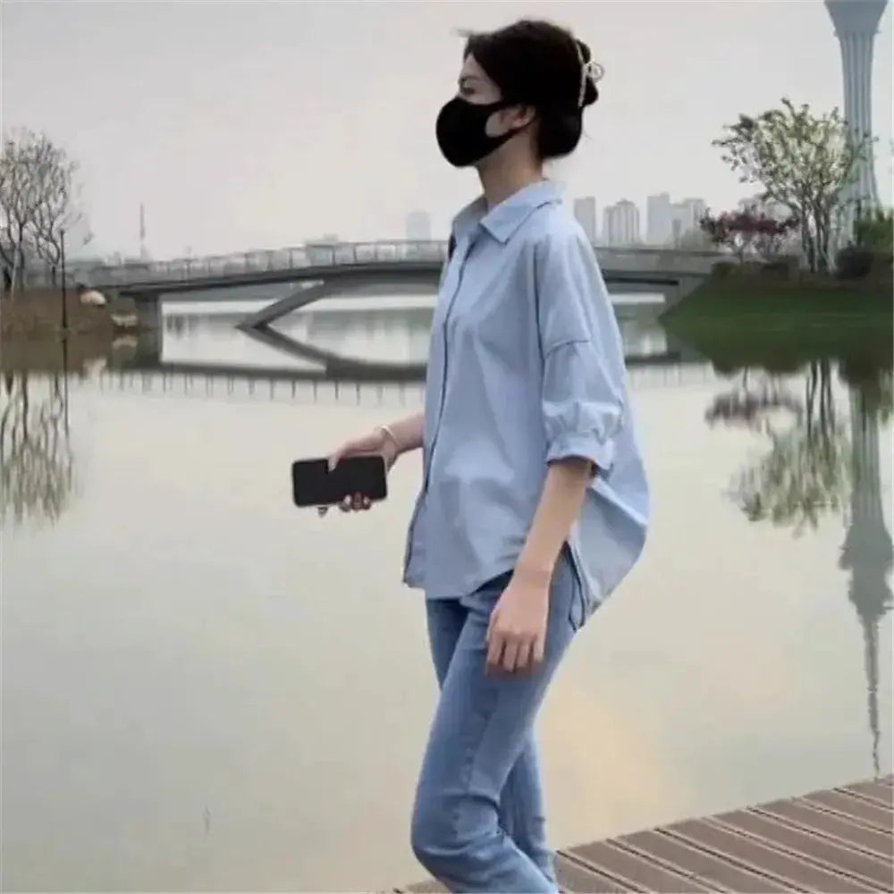 Women's light-blue loose mid-sleeve blouse with collar, paired with jeans outdoors by a lake