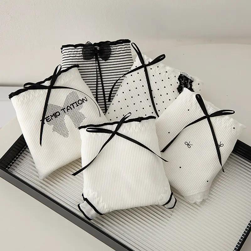 Six white ribbed women's panties with black bow accents, assorted styles on a display tray