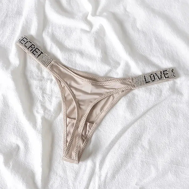 Beige low-rise thong with rhinestone embellished waistband spelling LOVE by Simples Market