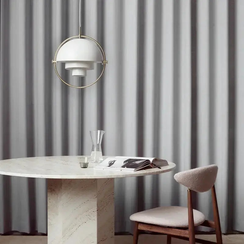 Pendant light with circular gold frame and white layered shade, hung above a marble round table