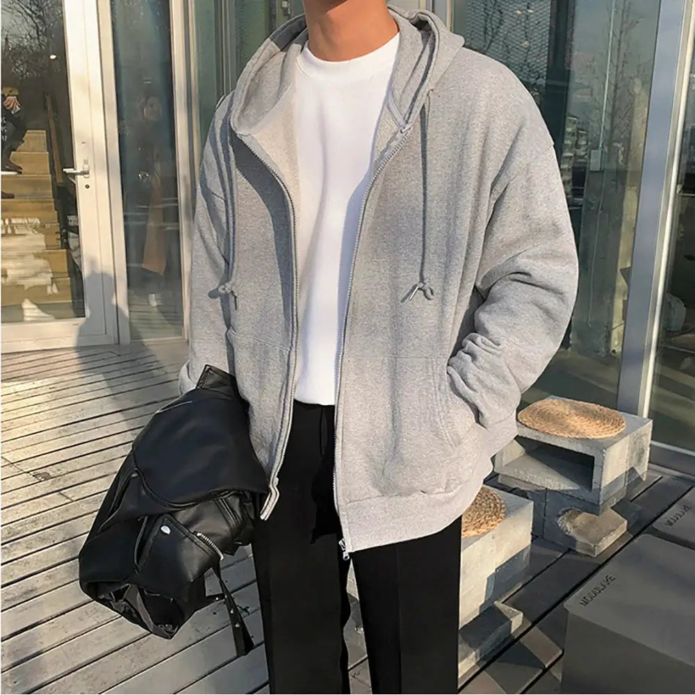 Gray zip-up hoodie worn over a white T-shirt; unisex casual fleece with drawstrings, holding a black leather jacket.