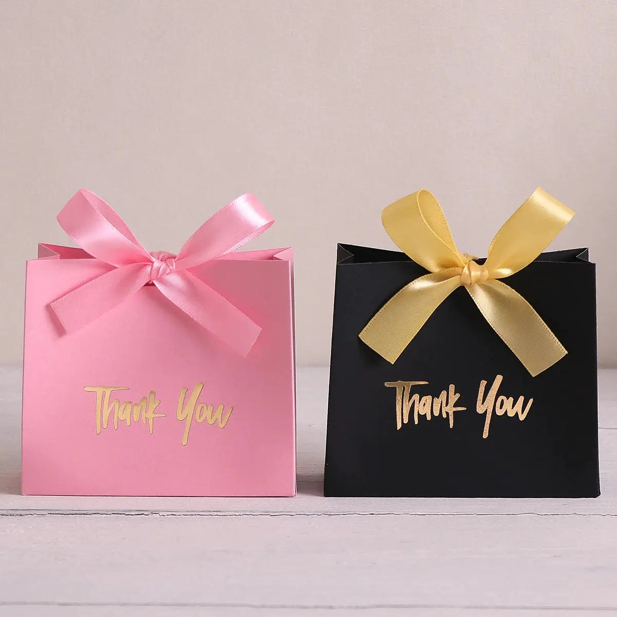Pink gift box with pink ribbon and black gift box with gold ribbon, both with gold Thank You text.