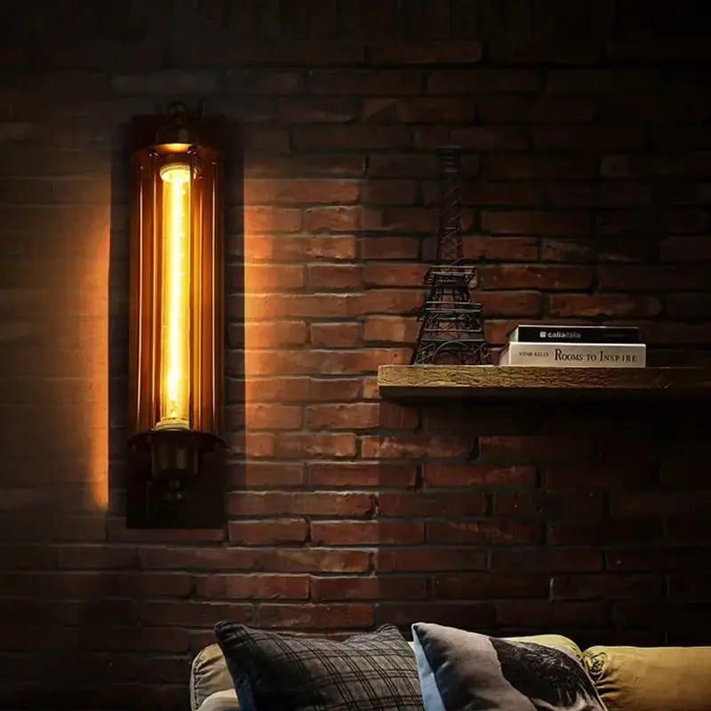 Retro industrial iron wall light with warm amber LED glow mounted on a brick wall beside a shelf and sofa.