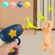Blue interactive cat training launcher with yellow star, shooting colorful discs as orange kitten leaps to catch them