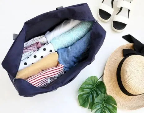 Large capacity travel bag navy fabric; opened to show folded clothes, with straw hat and white sandals nearby.