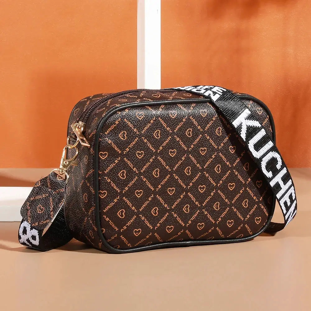 Crossbody bag in brown pattern with heart motif, gold-tone zippers, adjustable strap