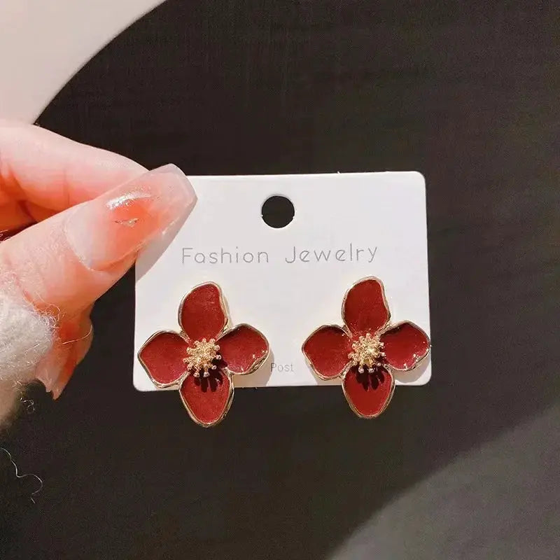 Red enamel flower stud earrings with gold-tone edges and center stones, pair on display card