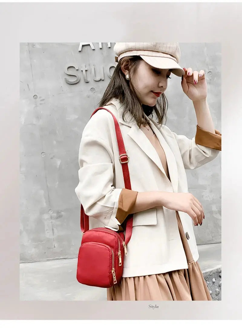 Red crossbody handbag with gold zippers worn by a woman in a beige blazer.