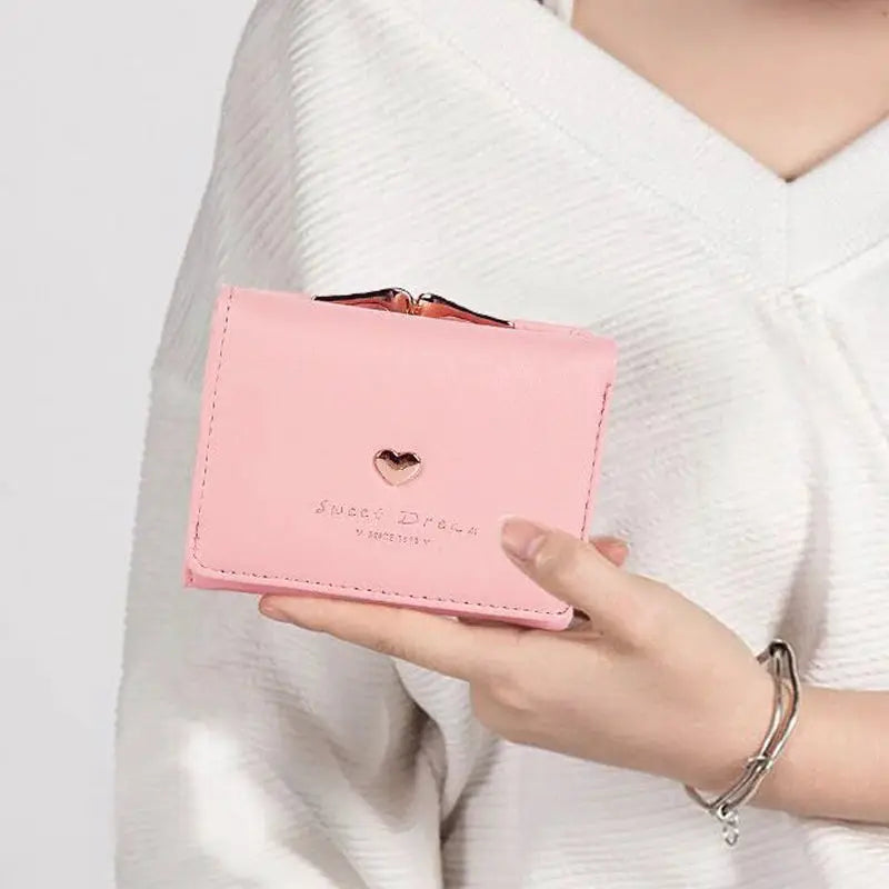 Pink mini folding wallet held in hand with a heart cutout on the front