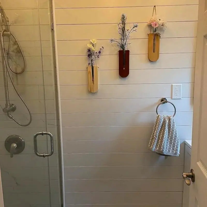 Three wooden hanging planters on a white paneled bathroom wall in natural, dark brown and light wood tones with dried stems.