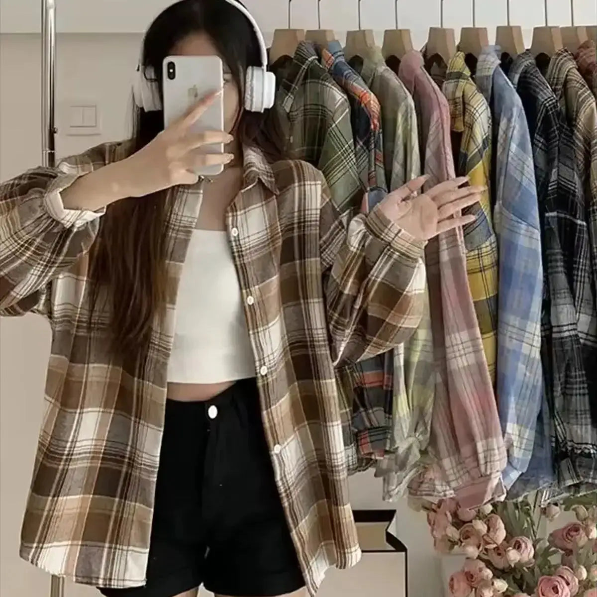 Brown plaid long-sleeve shirt worn open over a white crop top; rack of assorted plaid shirts in the background.