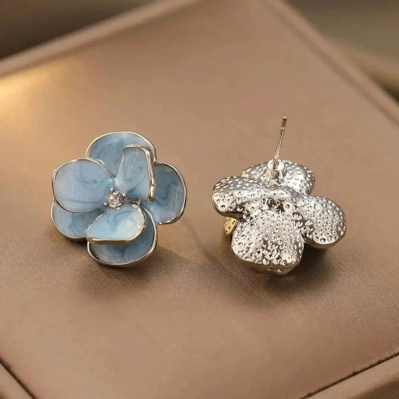 Simples Market blue enamel flower earrings with crystal center and silver outline; pair shown, one blue-enamel front and one textured silver bloom.