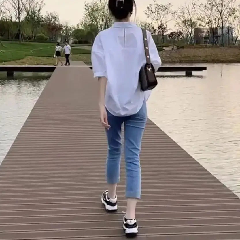 Women's light-blue loose summer blouse with mid sleeves, paired with cropped jeans and a crossbody bag
