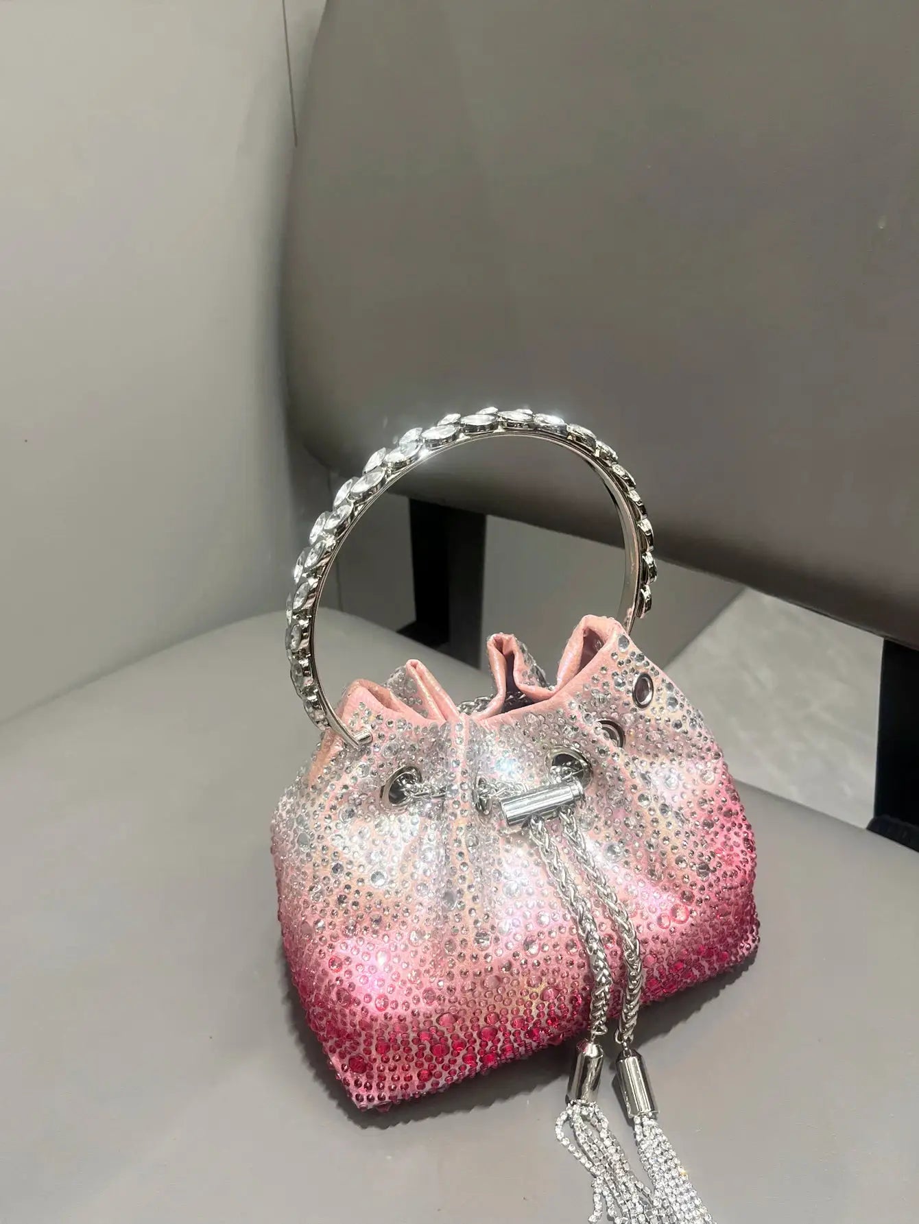 Crystal-embellished pink gradient bucket-style evening clutch with a silver ring handle and crystal tassel chain