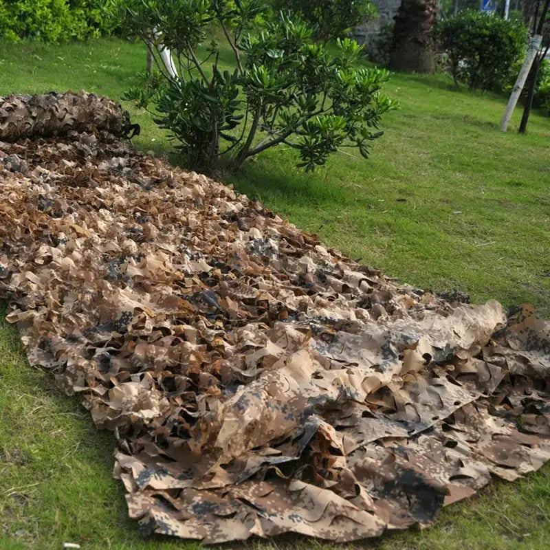 Military camouflage netting in desert tan/brown tones laid on grass.