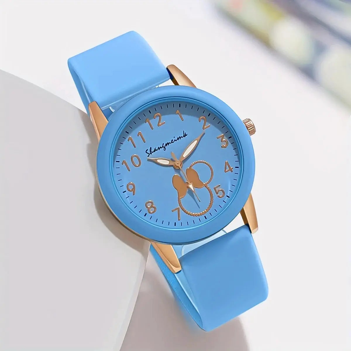 Women's blue silicone-band wristwatch with a round case and rose-gold accents; cartoon dial with gold numerals.
