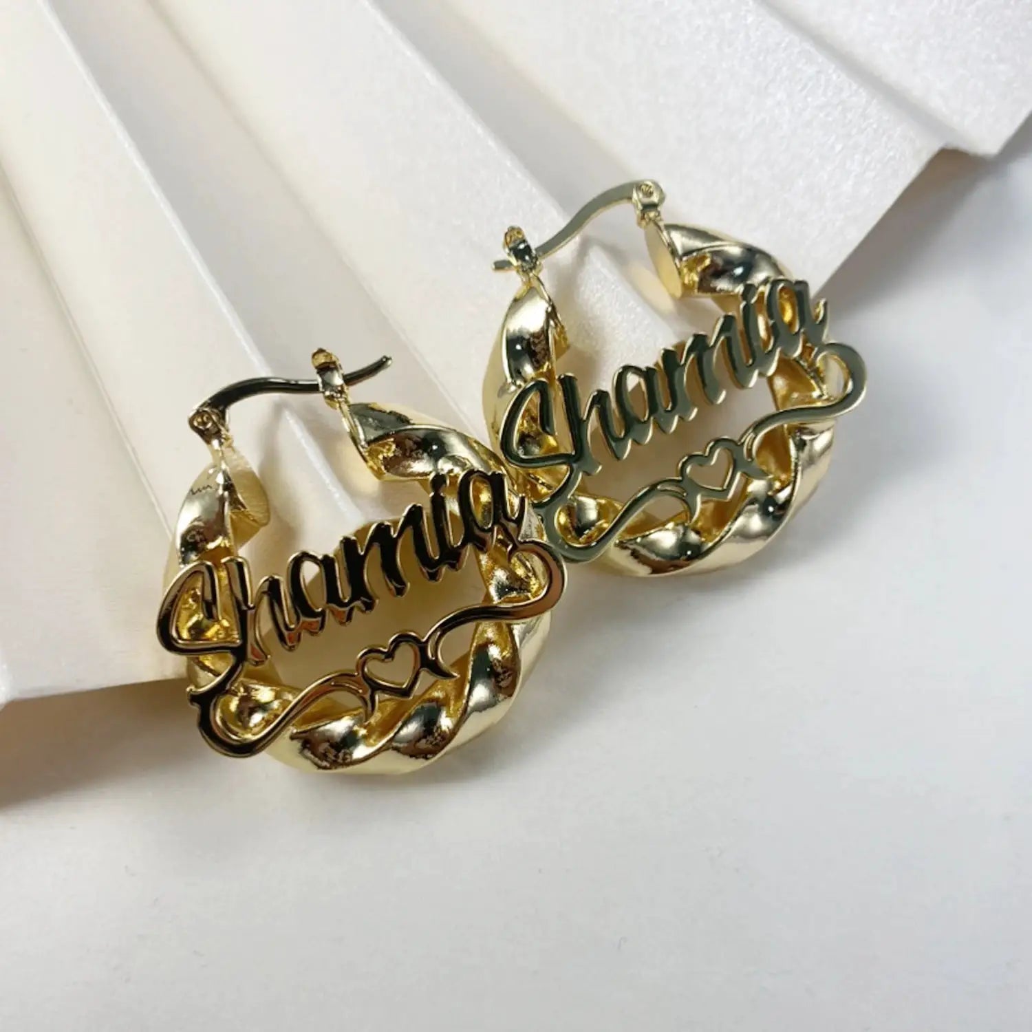 Pair of custom name hoop earrings in gold-tone metal with cursive name lettering and small heart accents.