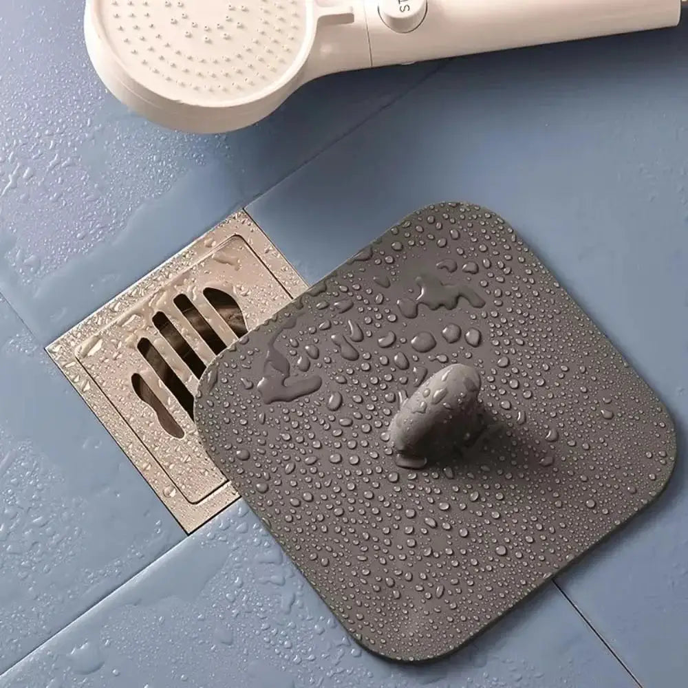 Simples Market silicone bathroom floor drain pad, gray square with central knob placed over a metal drain