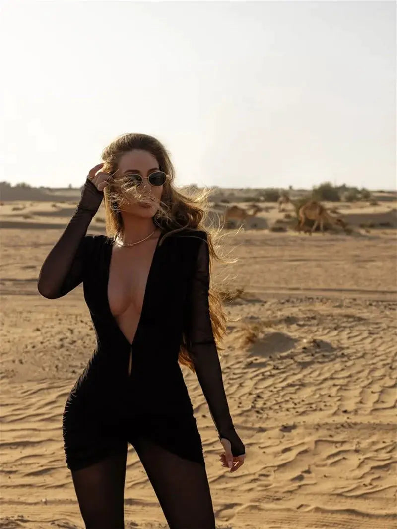 Jumpsuit, black deep-V long-sleeve with sheer mesh sleeves and a form-fitting silhouette in a desert setting.