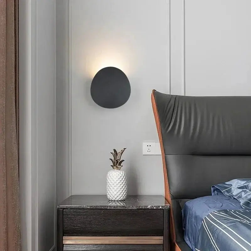 Simples Market outdoor LED wall lamp, black round sconce with upward glow beside a gray-walled bedroom.