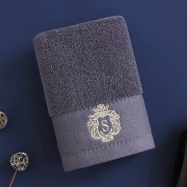 Towel set with gold-embroidered crest, dark gray towels rolled on a blue backdrop