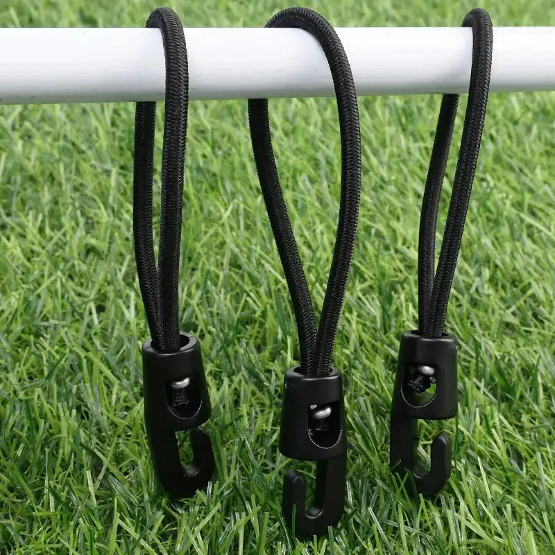 Three black elastic bungee cords with hooks hanging from a white bar over grass.
