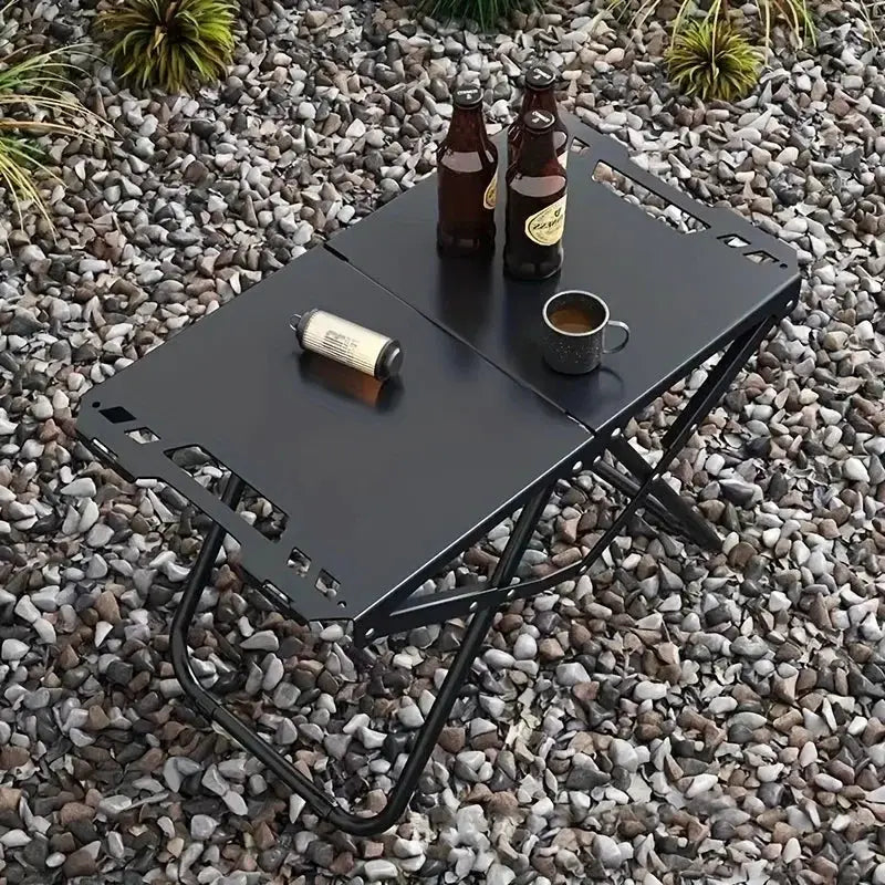 Simples Market portable folding camping table, black stainless steel; two beer bottles and a mug on top.