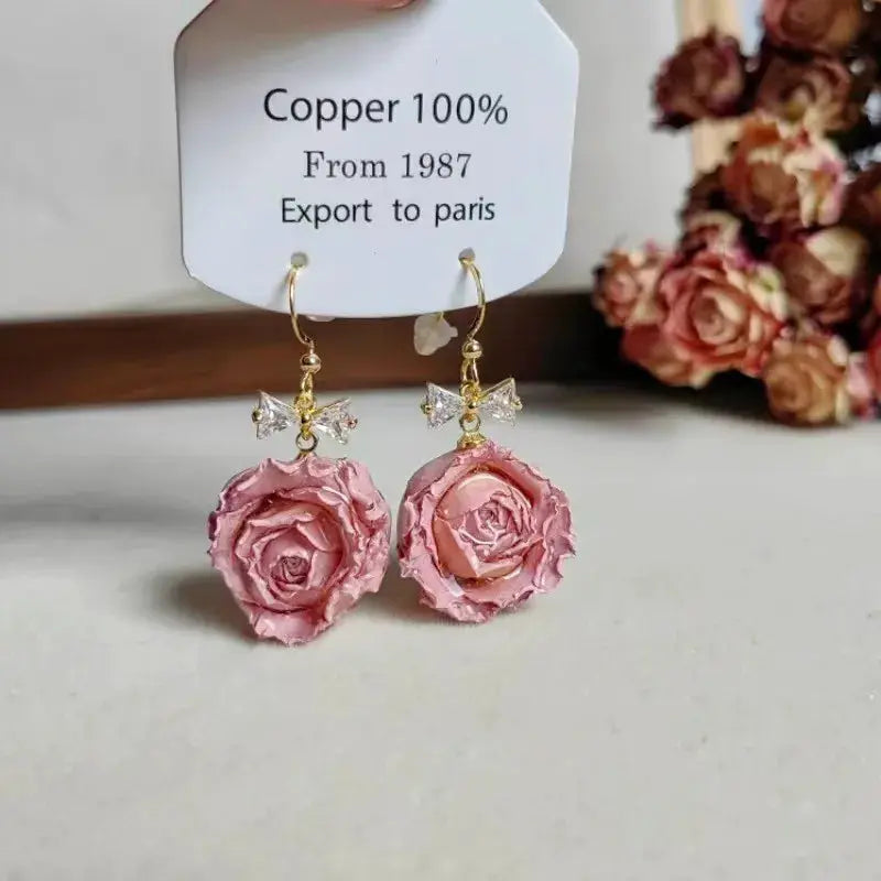 Pair of pink rose epoxy resin drop earrings with crystal bow accents on gold hooks