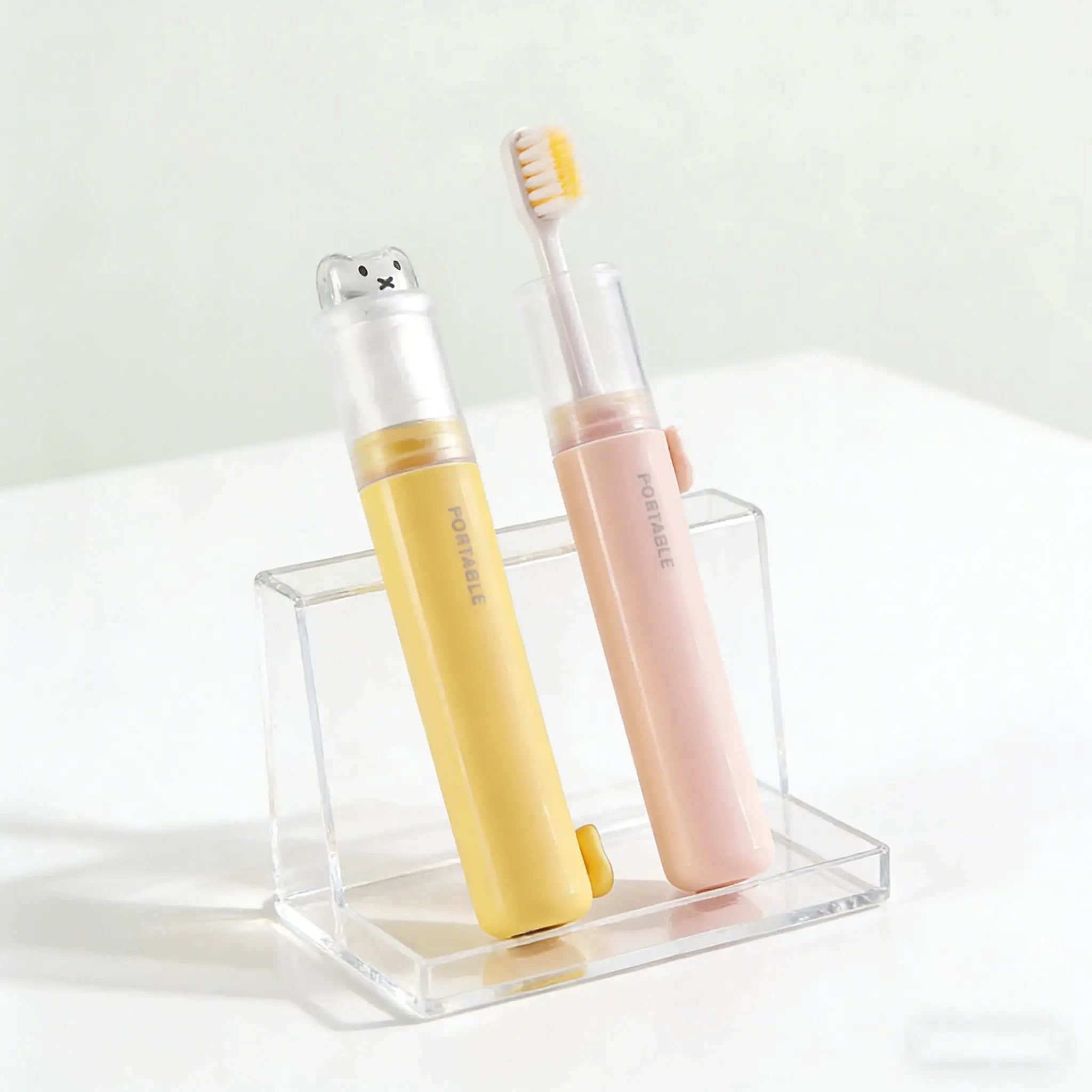 2-in-1 foldable travel toothbrushes (2-pack) with bear-shaped dust covers in pastel yellow and pink macaron colors