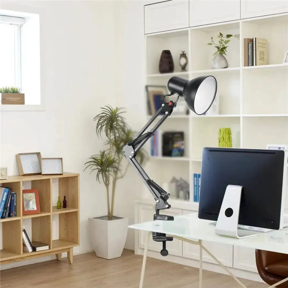 Swing arm clamp desk lamp, black metal with adjustable arms, mounted on a glass desk in a bright office.