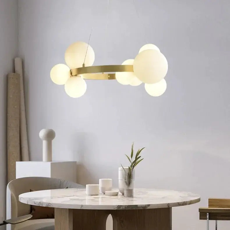 Simple chandelier hanging lamp with a gold-finish ring and frosted glass globes above a marble table