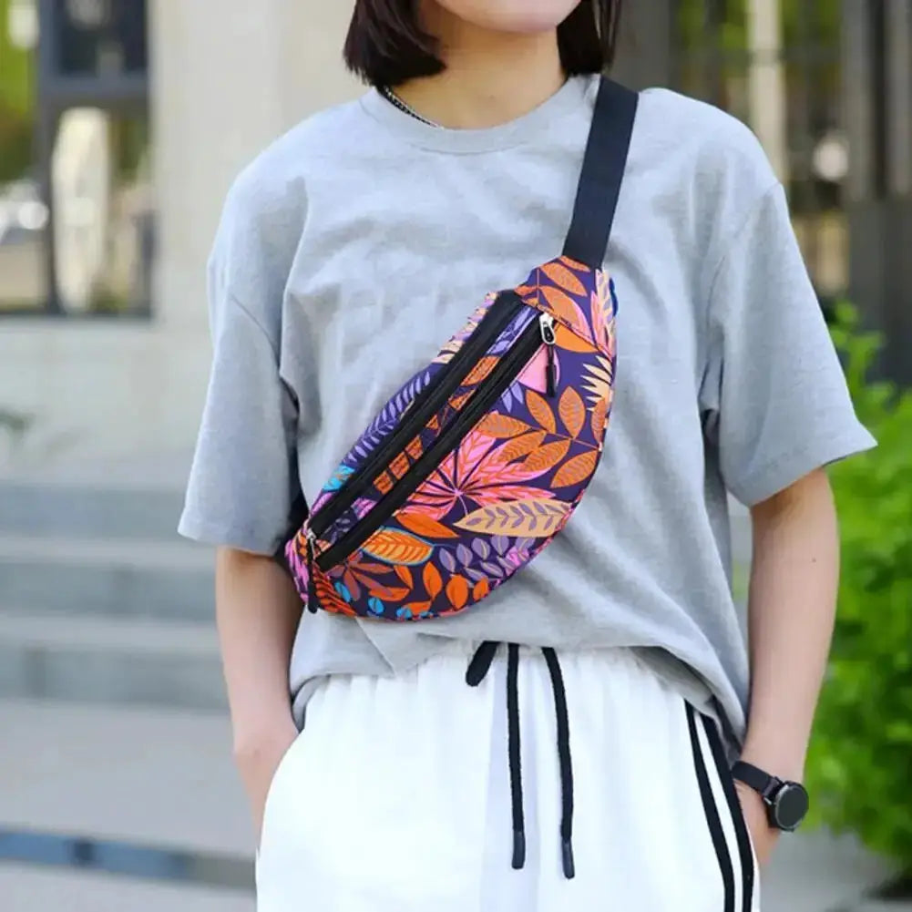 Sports waist pack with tropical leaf print in purple, orange, pink; worn crossbody with black strap