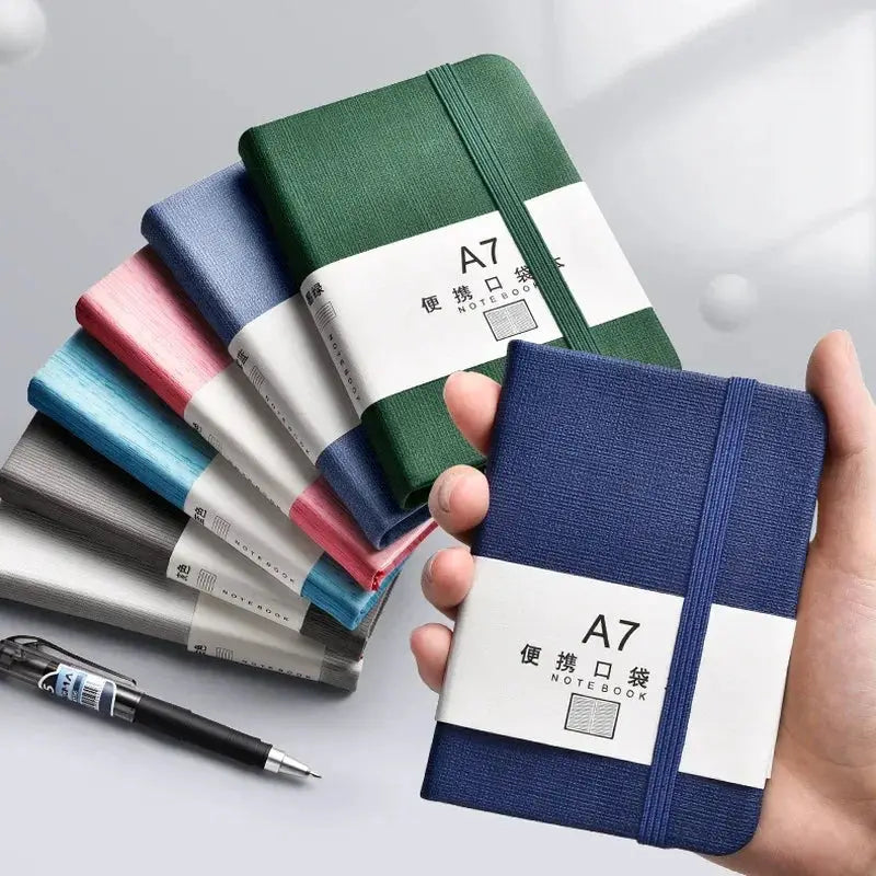 A7 mini notebook; blue held in hand among 8-color assortment of pocket notebooks with elastic straps.