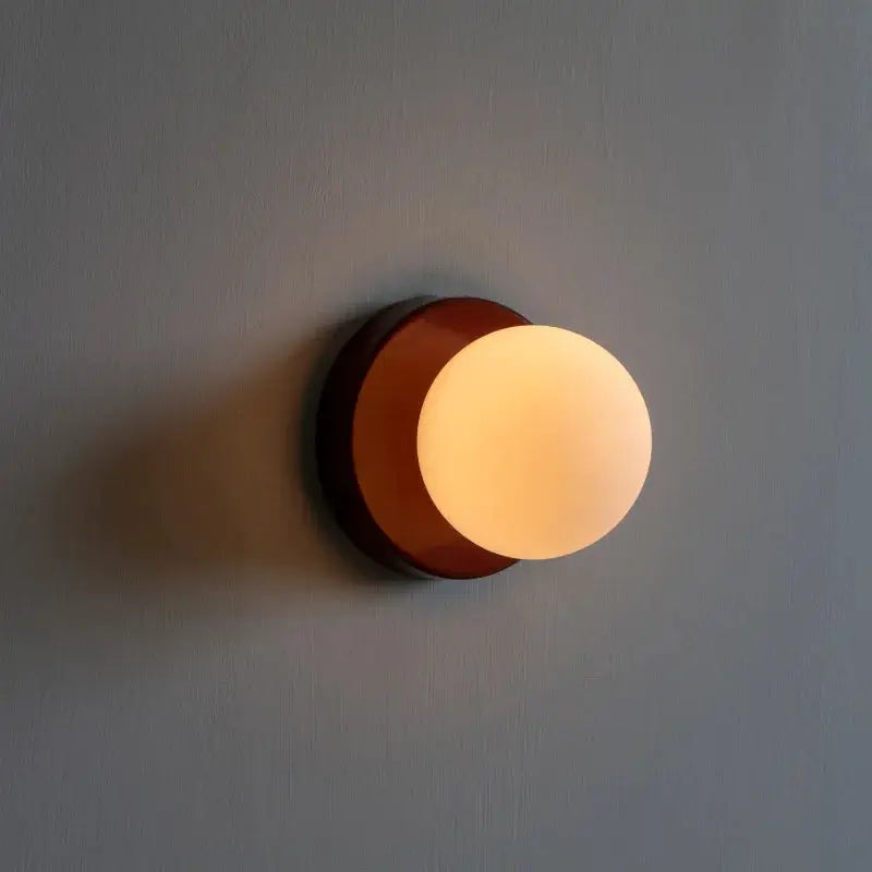 Macaron wall lamp with brown iron base and white plastic globe lampshade.