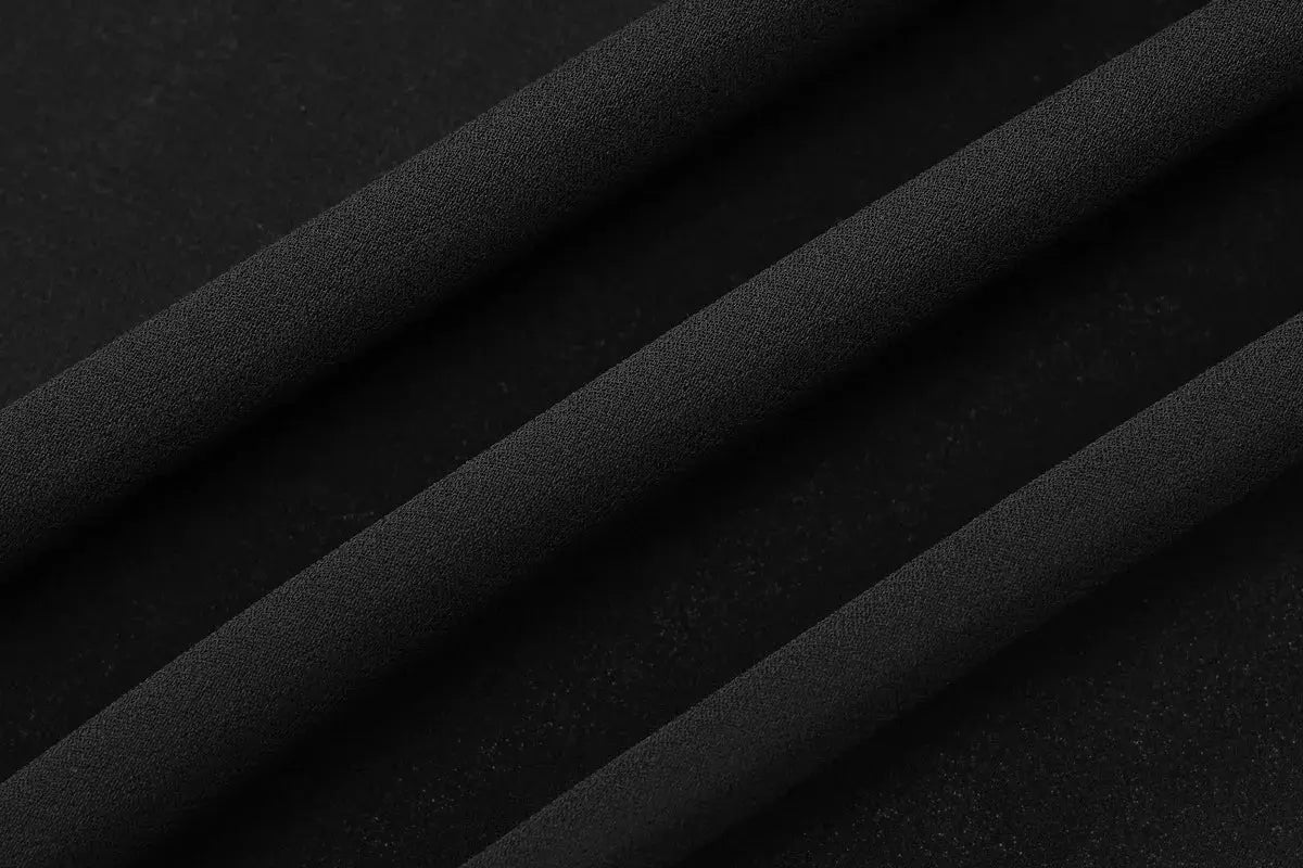 Chiffon blouse fabric in black close-up with diagonal folds and smooth texture