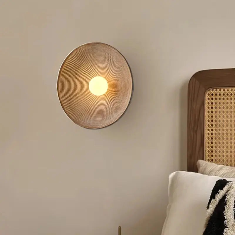 Retro Japanese resin wall lamp, round ribbed shade in warm brown, emits cozy ambient light beside the bed
