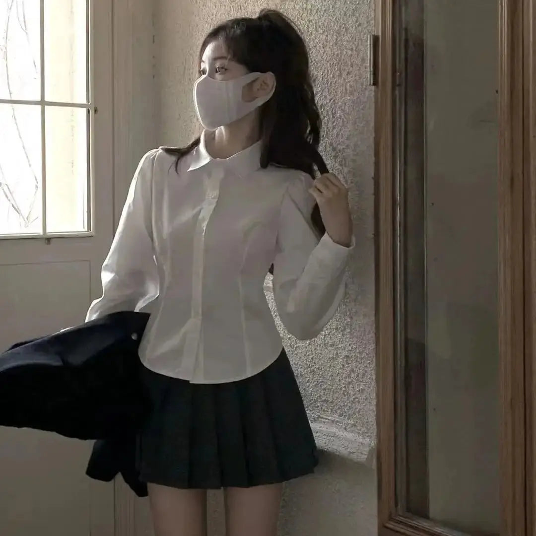White women's button-down shirt with slim long sleeves from Simples Market; paired with a black pleated skirt.