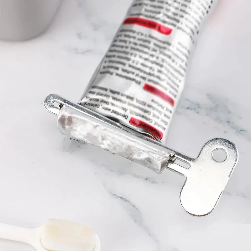Stainless steel toothpaste squeezer tool clamped to a toothpaste tube; bathroom cosmetic accessory.