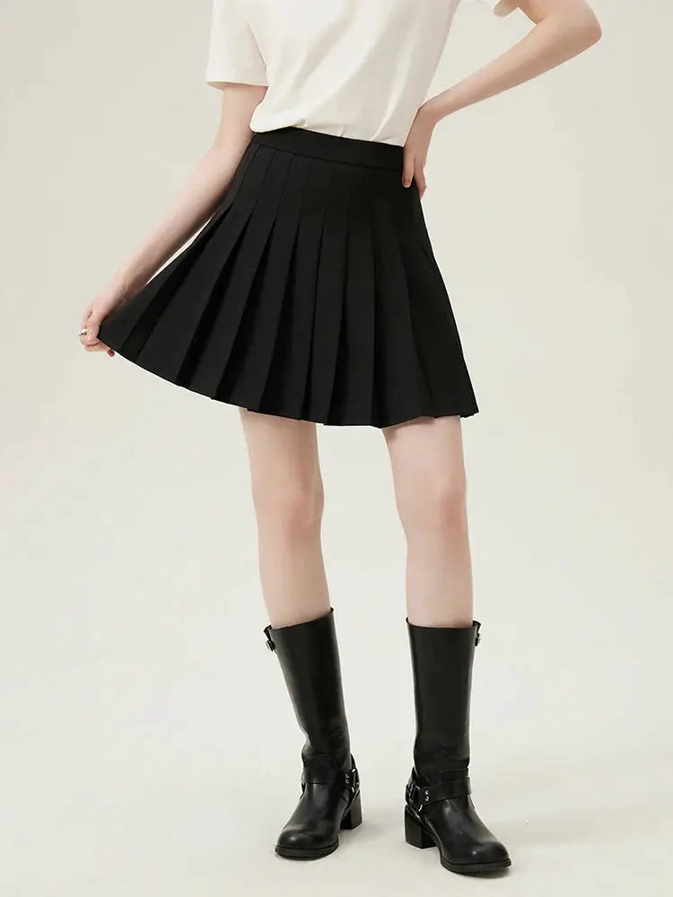 Black pleated mini skirt on a model, paired with a white top and black knee-high boots
