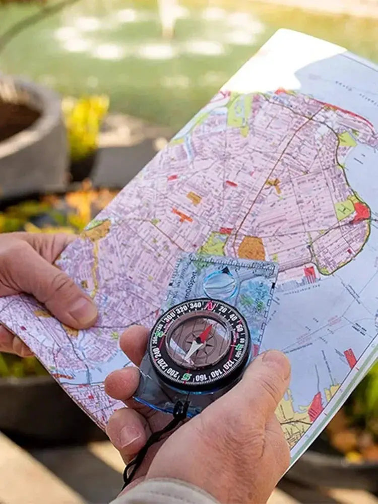 Waterproof compass, black with red needle, held over a colorful map for outdoor hiking navigation.