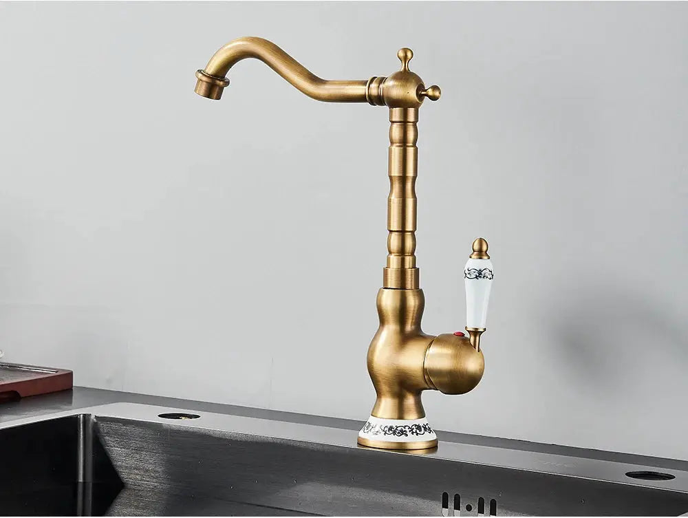 Antique brass faucet with rotating spout and white ceramic handle on a sink