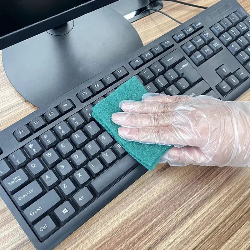 Disposable TPE gloves, clear, used to clean a keyboard with a green sponge