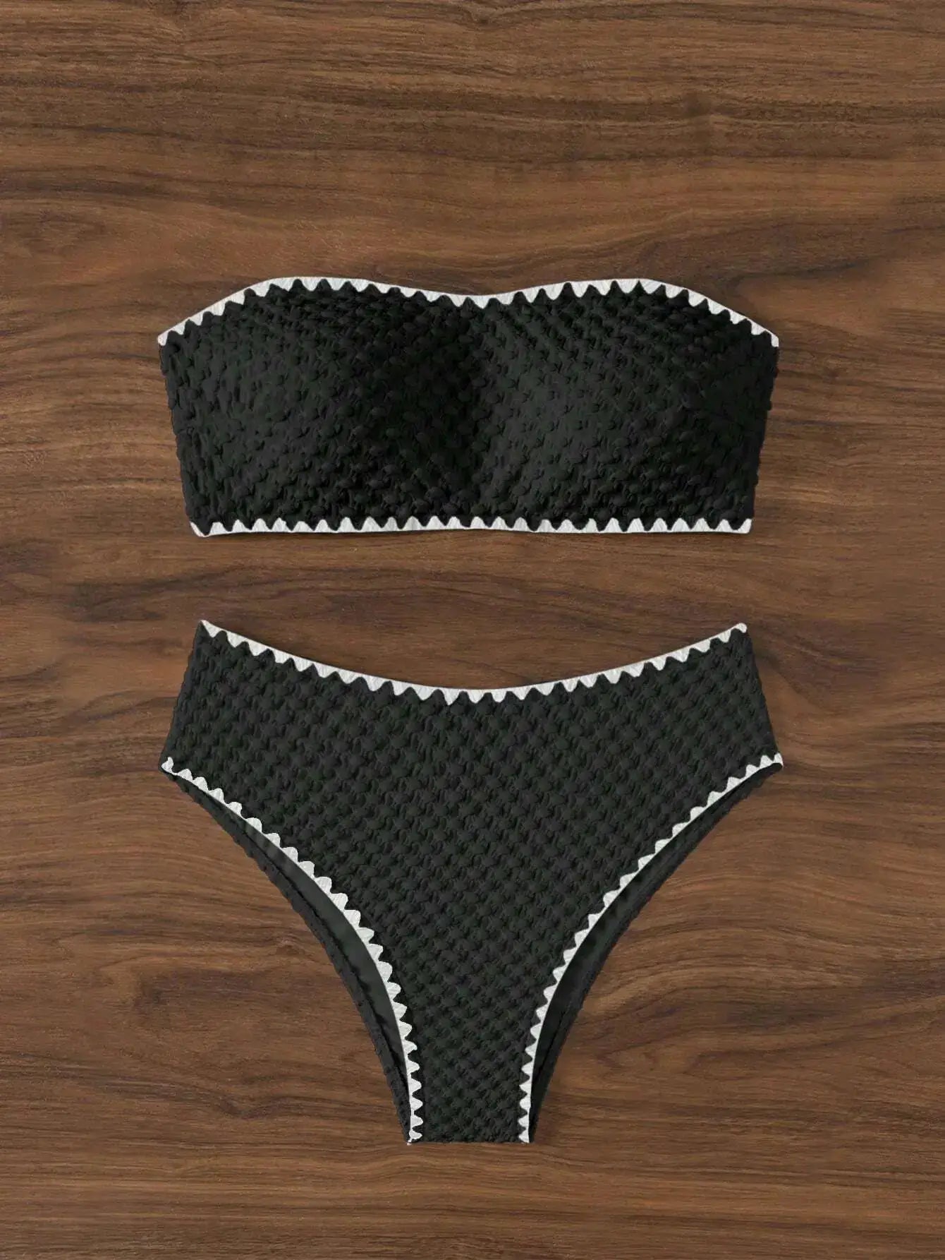 Two-piece black strapless bikini set with white zigzag trim, bandeau top and high-cut bottom on wood background