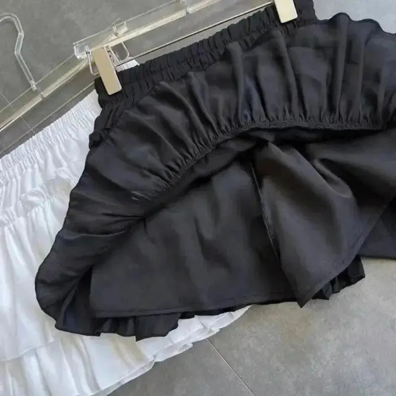 Black mini A-line skirt with elastic waist and layered ruffle hem; white skirt behind (2 skirts shown).