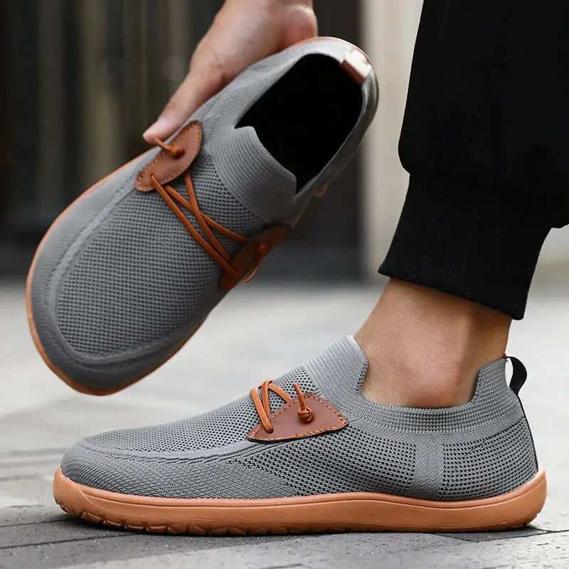 Pair of grey wide barefoot shoes with breathable mesh, tan leather lace accents, and gum sole