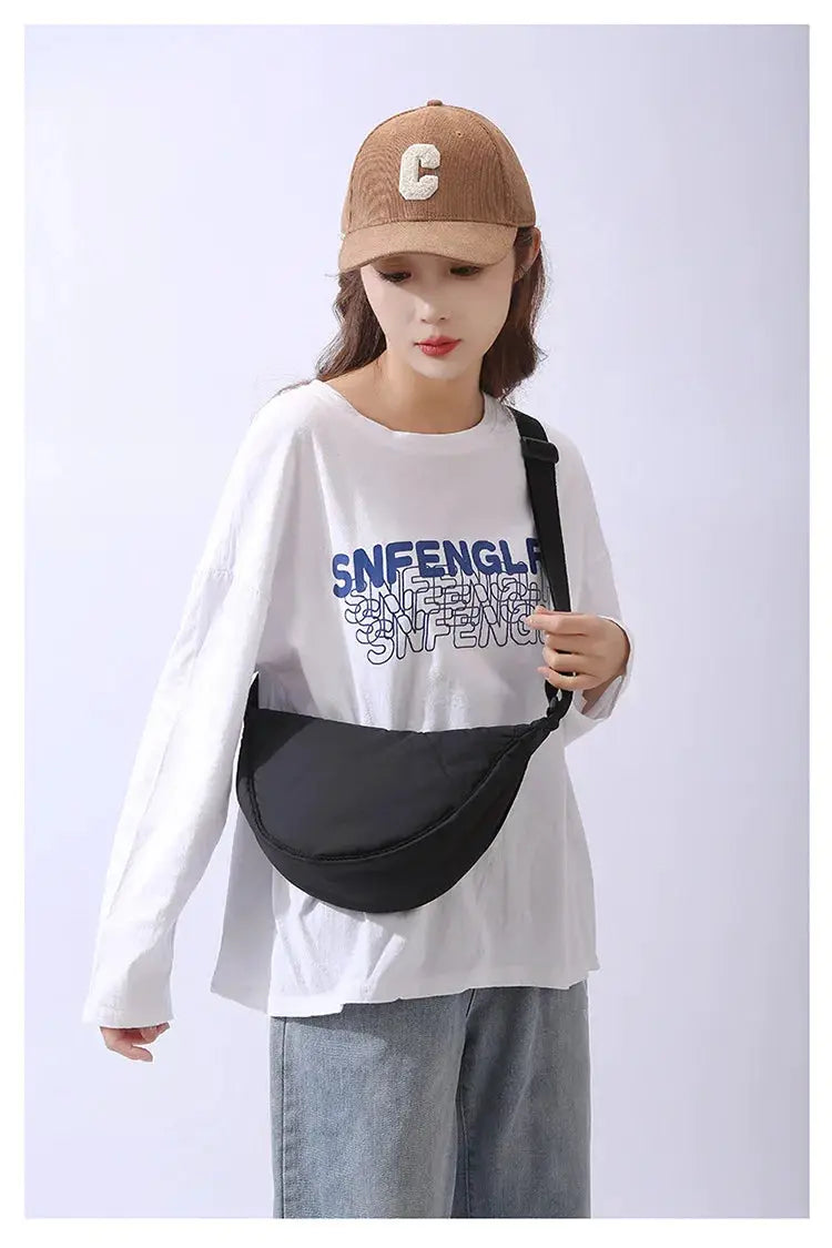Crossbody bag in black nylon with adjustable strap, worn by model over a white tee.